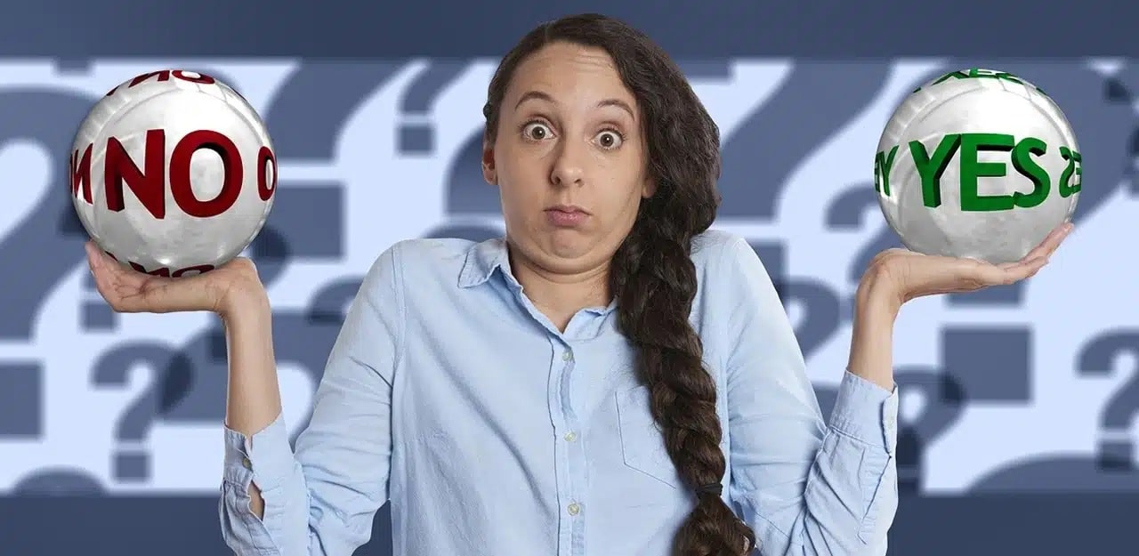 A confused looking woman in a blue shirt holding a ball with No written on it in her left hand and a ball with Yes on it in her right hand.