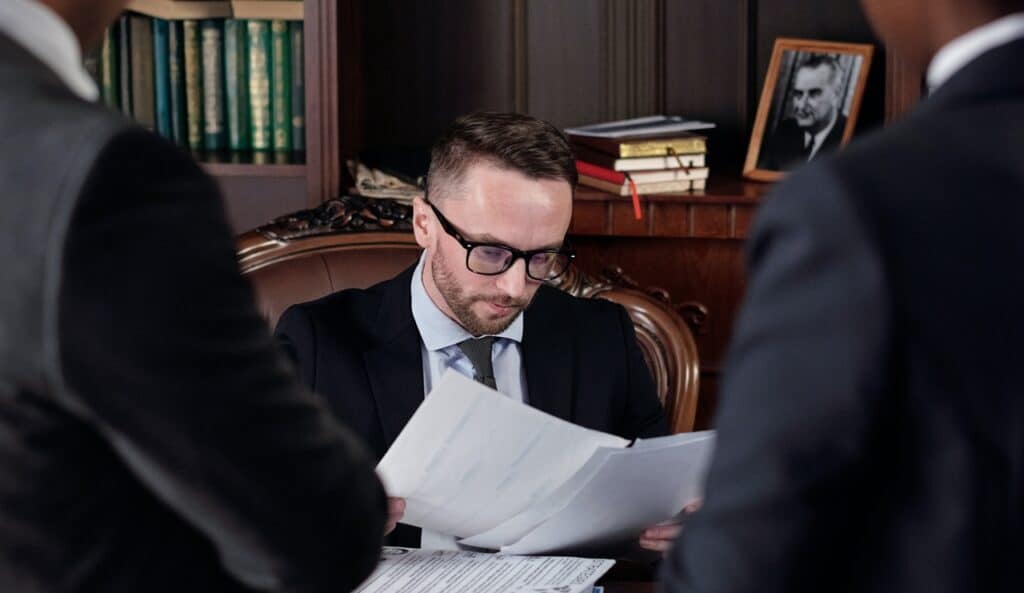 A lawyer sat at his desk checking the details of a Last Will and Testament with 2 people waiting. A Notarial Will Philippines does have advantages.