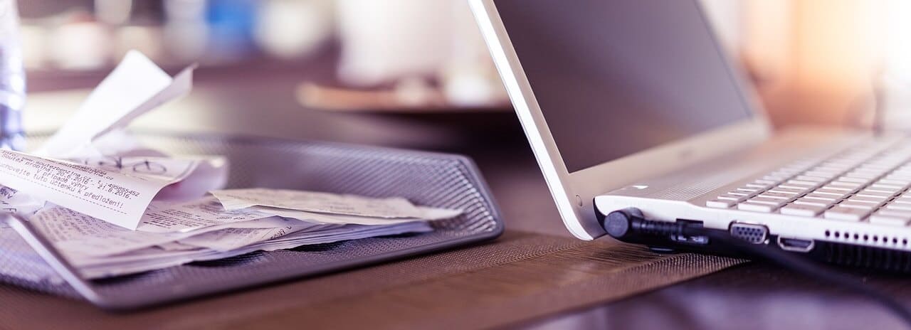 Pile of receipts beside a laptop symbolizing VAT.