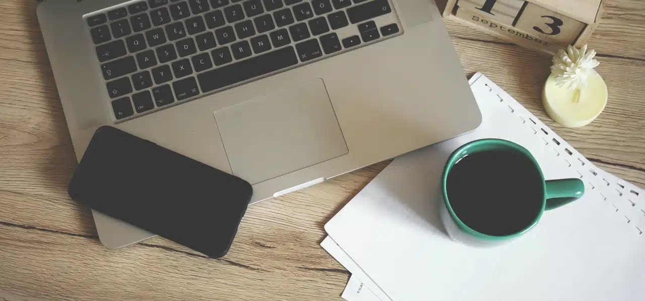 A cup of coffee over some documents beside a computer and a phone