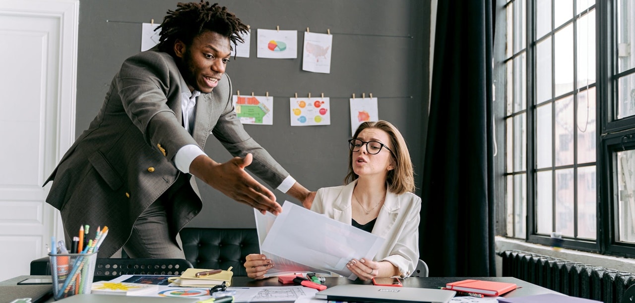 A man complaining to a woman on her desk