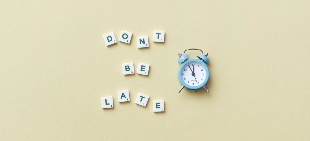 Scrabble tiles spelling the words Don’t Be Late with an alarm clock beside it